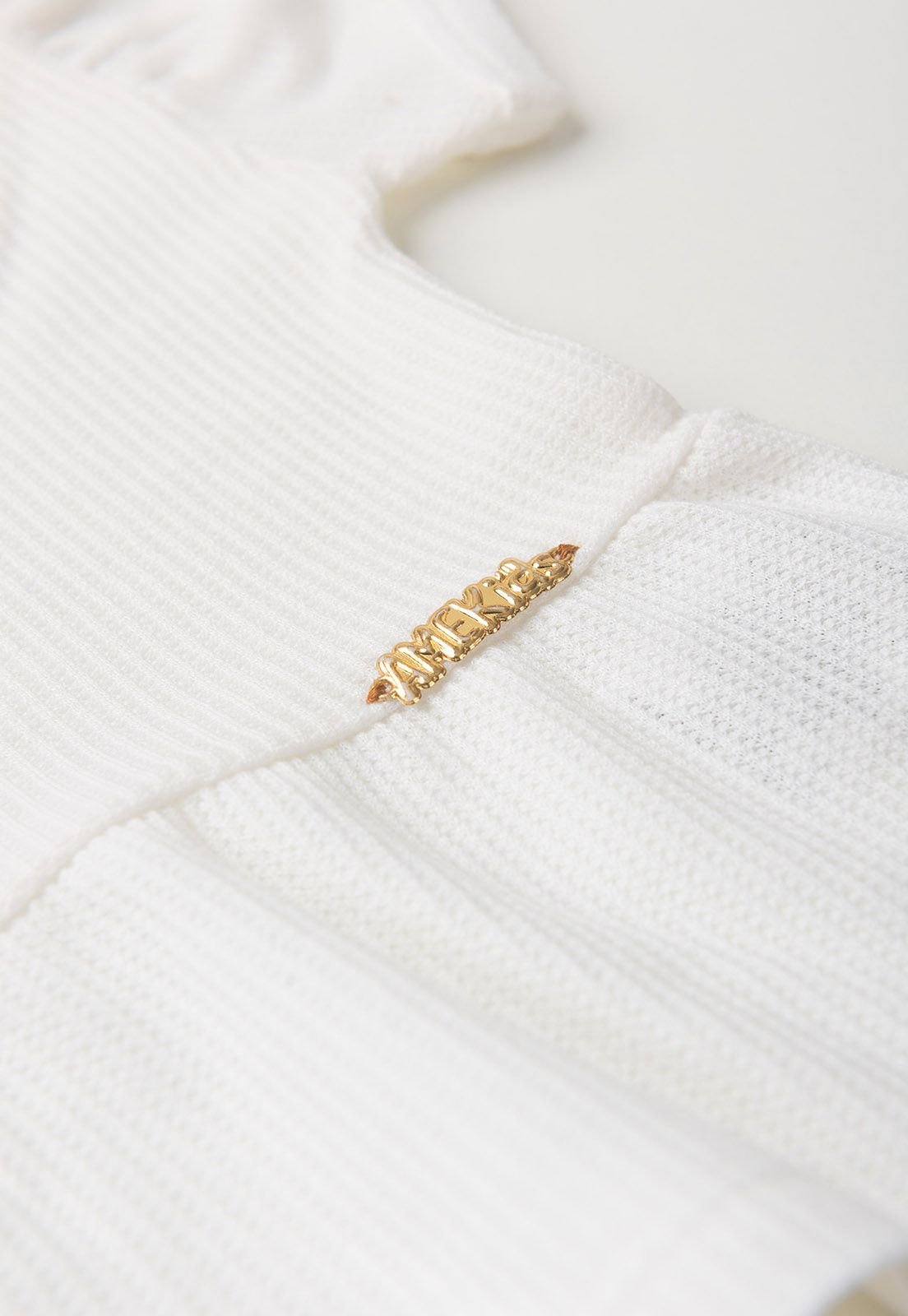 Detalhe: Plaquinha dourada do Conjunto Blusa e Shorts Moscou Ame Kids, cor Off-white